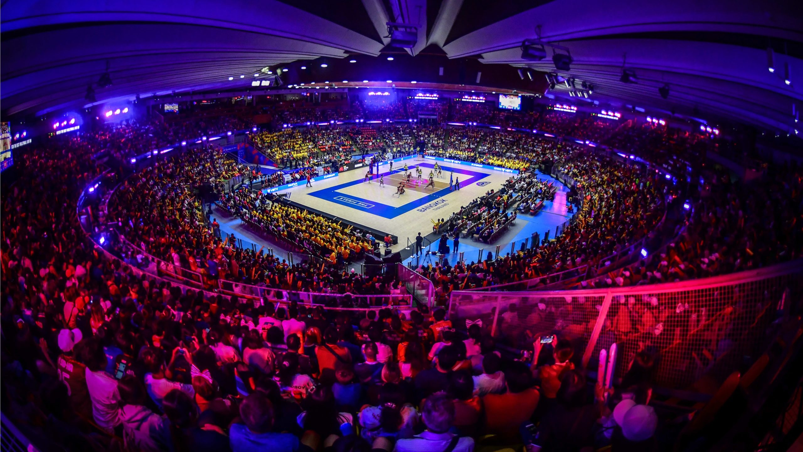 Packed indoor stadium with vibrant lights during a professional volleyball match.