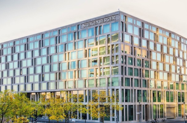 Modern exterior view of the Steigenberger Hotel building with grid-like architecture and reflective glass windows, surrounded by autumn trees.
