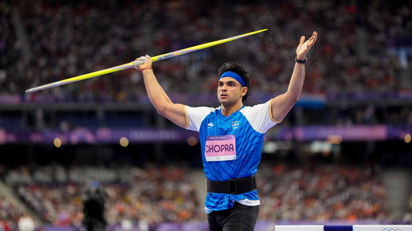 Neeraj Chopra prepares to throw javelin at Paris 2024 Olympics, representing India in track and field event with intense focus in front of a packed stadium crowd.