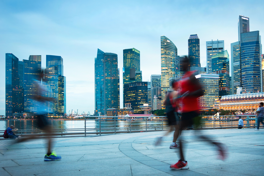 Joggers running along Marina Bay waterfront with Singapore skyline in the background.