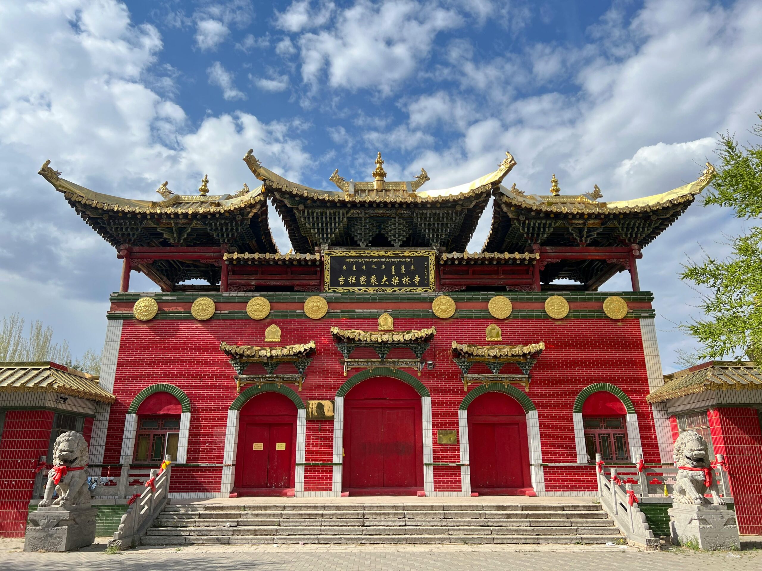 Traditional Chinese temple with ornate golden rooftops, red brick walls, and stone guardian lions under a partly cloudy sky.