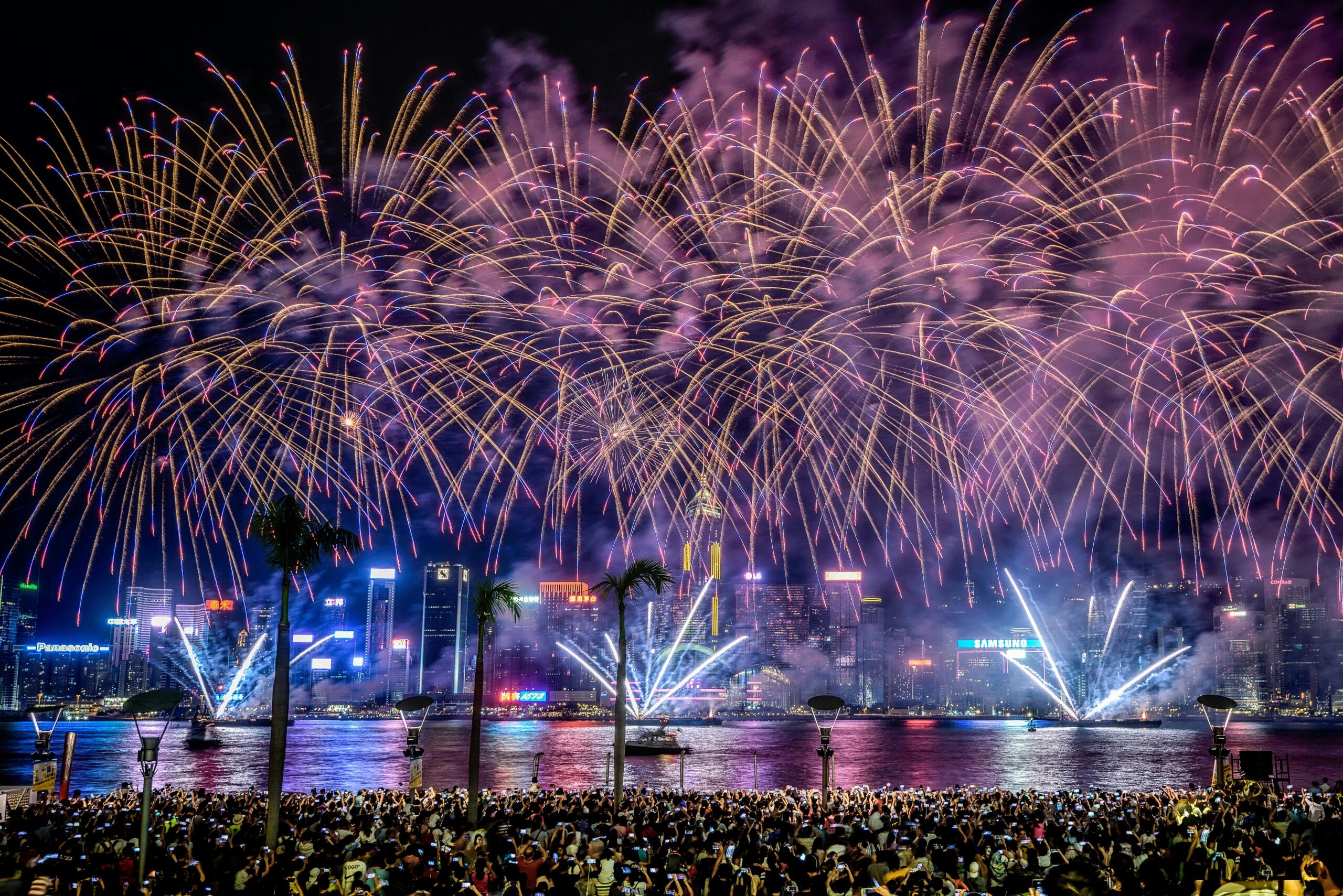 Spectacular fireworks display over Victoria Harbour in Hong Kong with a large crowd gathered along the waterfront during a night city celebration.