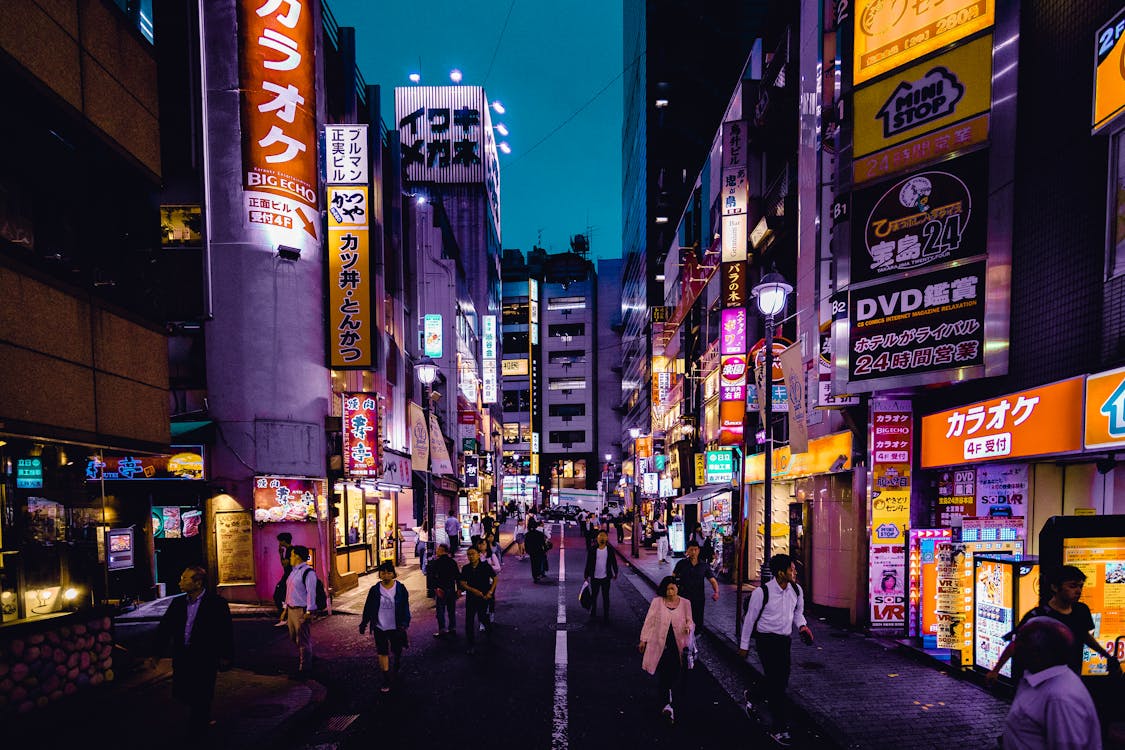 Busy nightlife street in Tokyo, Japan, illuminated by colorful neon signs and filled with people walking past restaurants, shops, and entertainment venues.