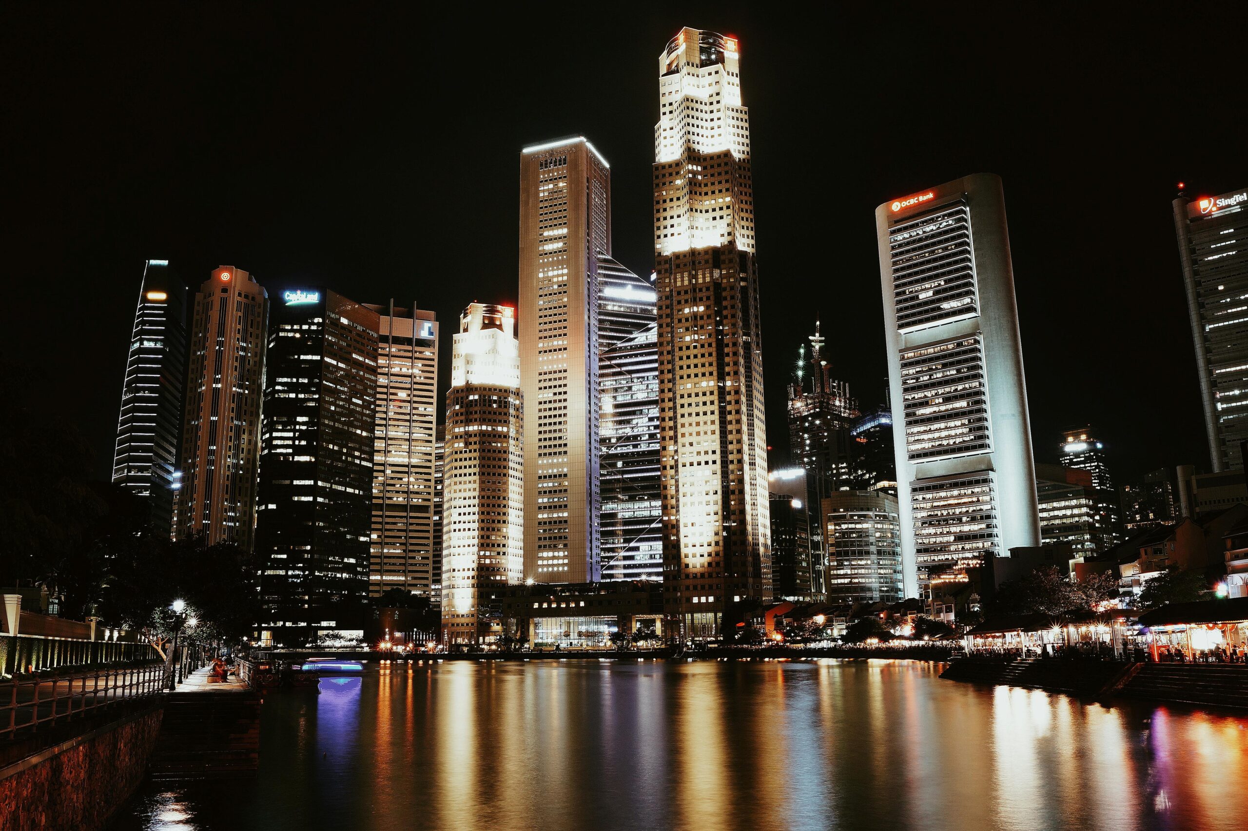 Nighttime cityscape of Singapore’s Central Business District with illuminated skyscrapers reflecting on the Singapore River.