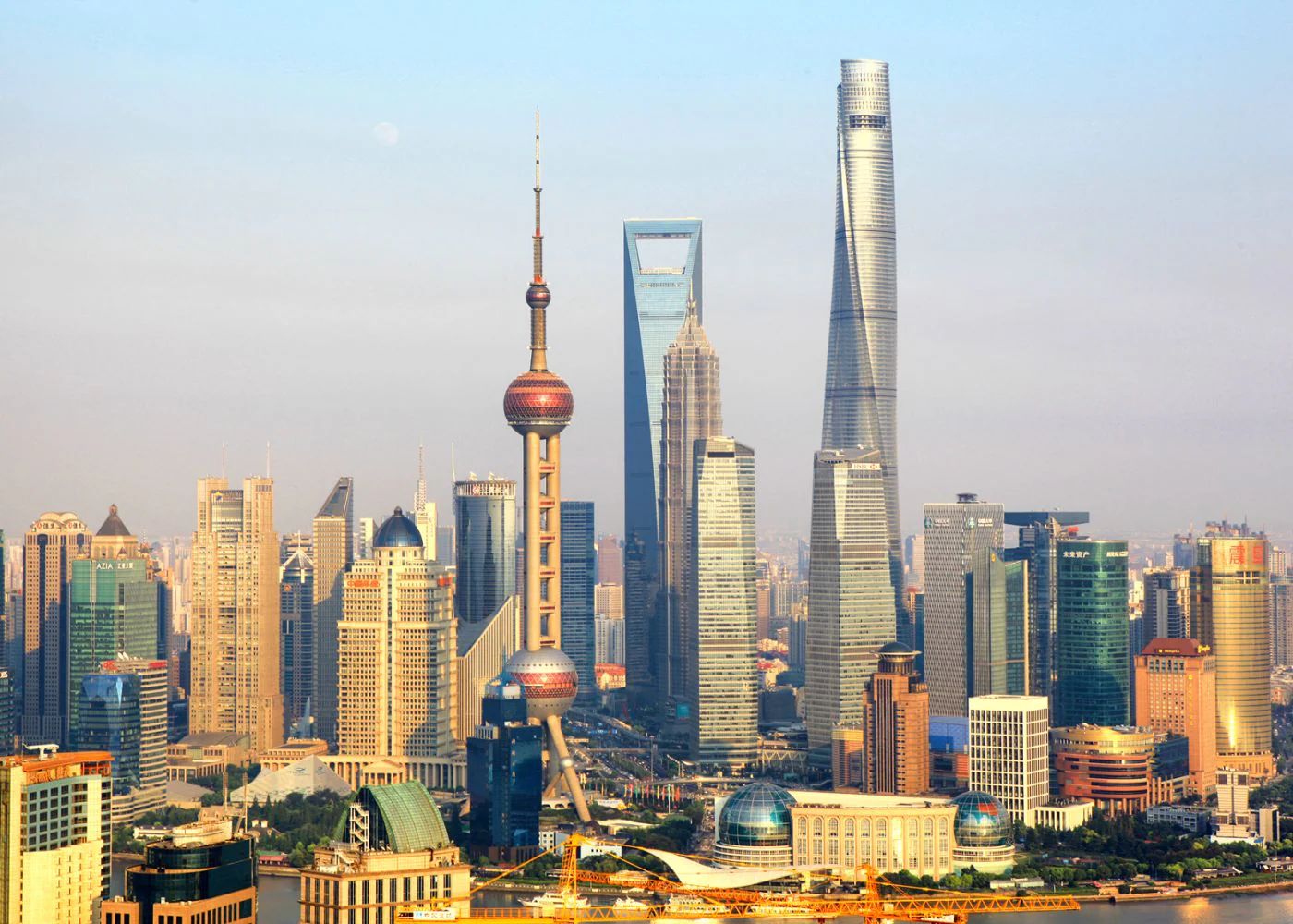 Panoramic view of the Shanghai skyline featuring the Oriental Pearl Tower, Shanghai World Financial Center, and Shanghai Tower under a clear sky.