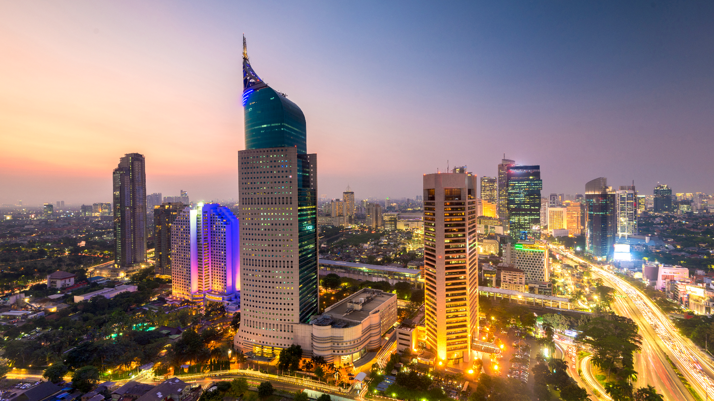 Jakarta city skyline at dusk with Wisma 46 skyscraper illuminated and traffic trails along Sudirman Central Business District in Indonesia